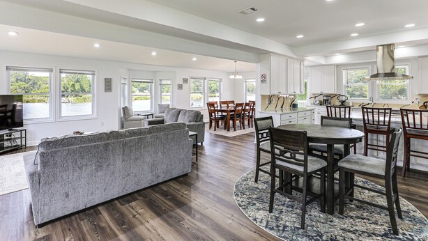 A spacious living area with a sofa, dining table, and chairs, large windows, and a kitchen area. - Modern Waterfront Home w/ Dock & Views in Deale (Deale)
