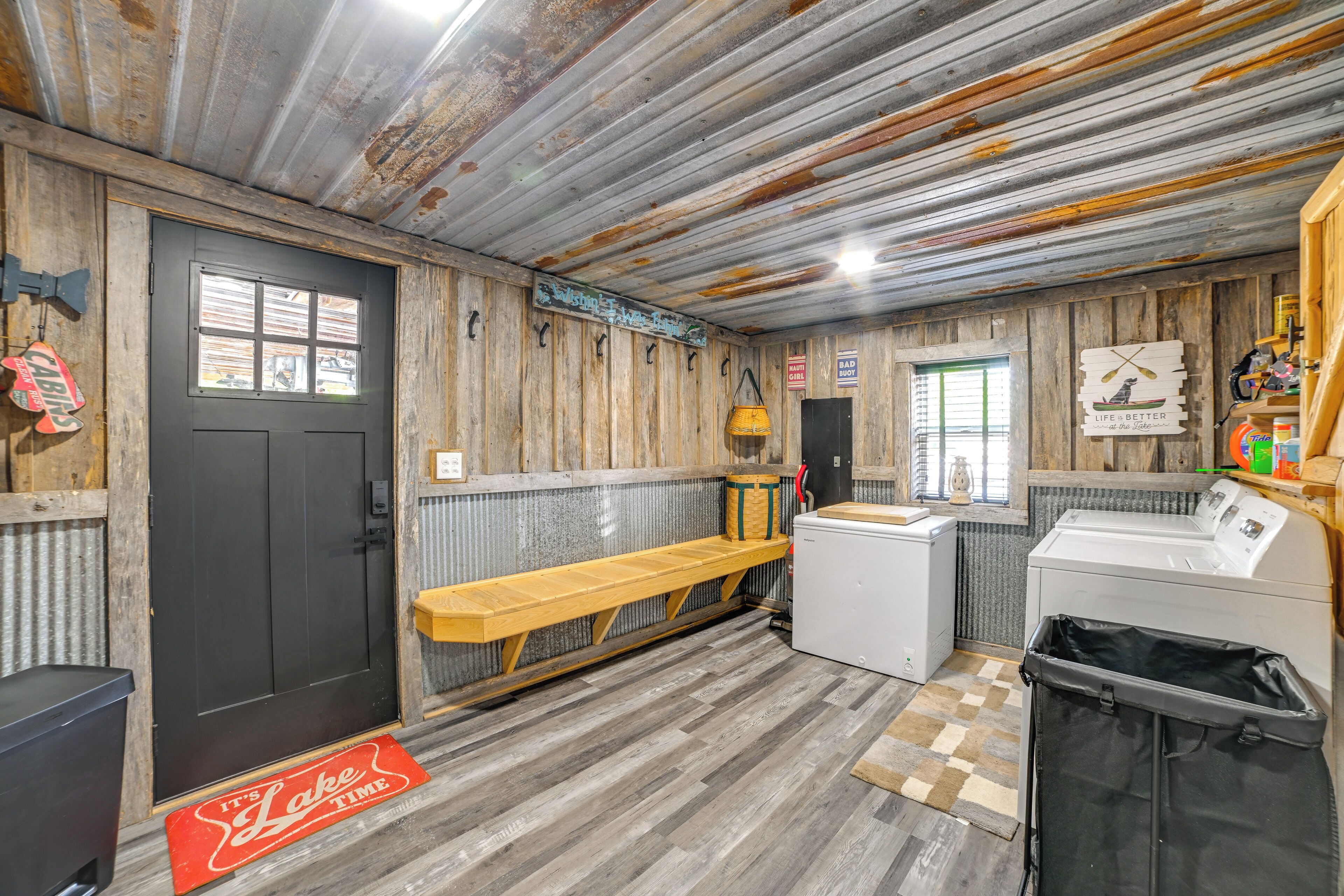 A rustic cabin interior with a wooden bench, a washing machine, and a trash bin.