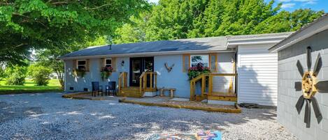 A single-story building with a porch, a gravel driveway, and a small outdoor seating area.