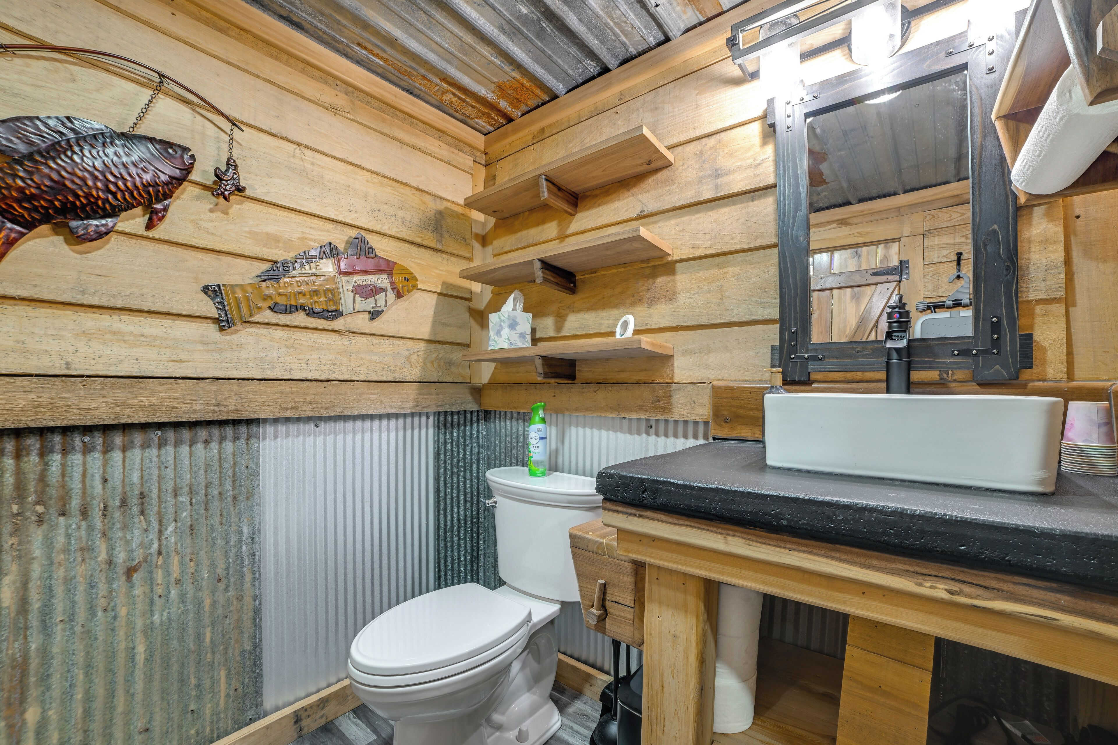 A wooden interior with a toilet, a shelf with a tissue box, a mirror, and a fish decoration.