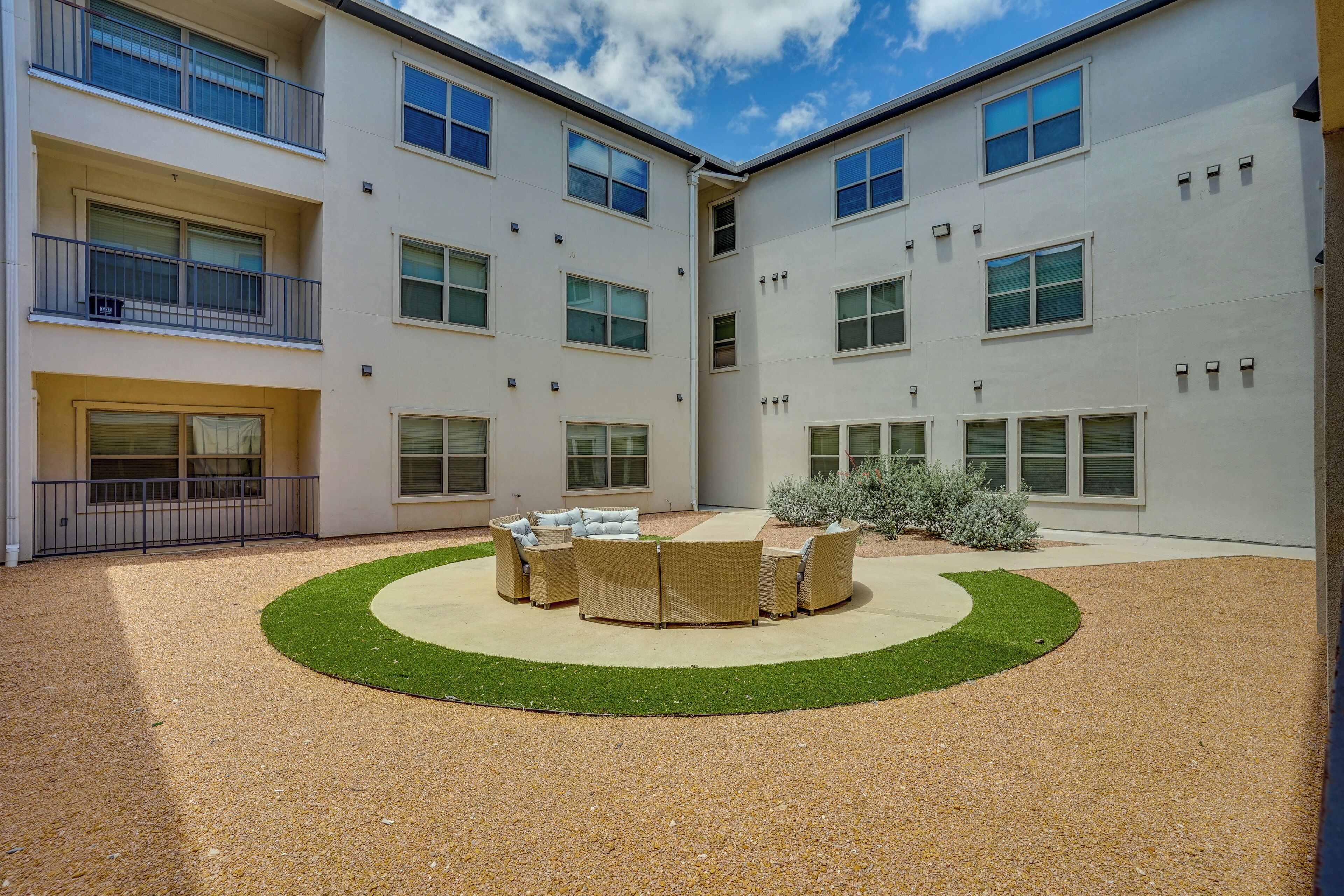 A courtyard with a circular seating area, a building with multiple windows, and a small garden.