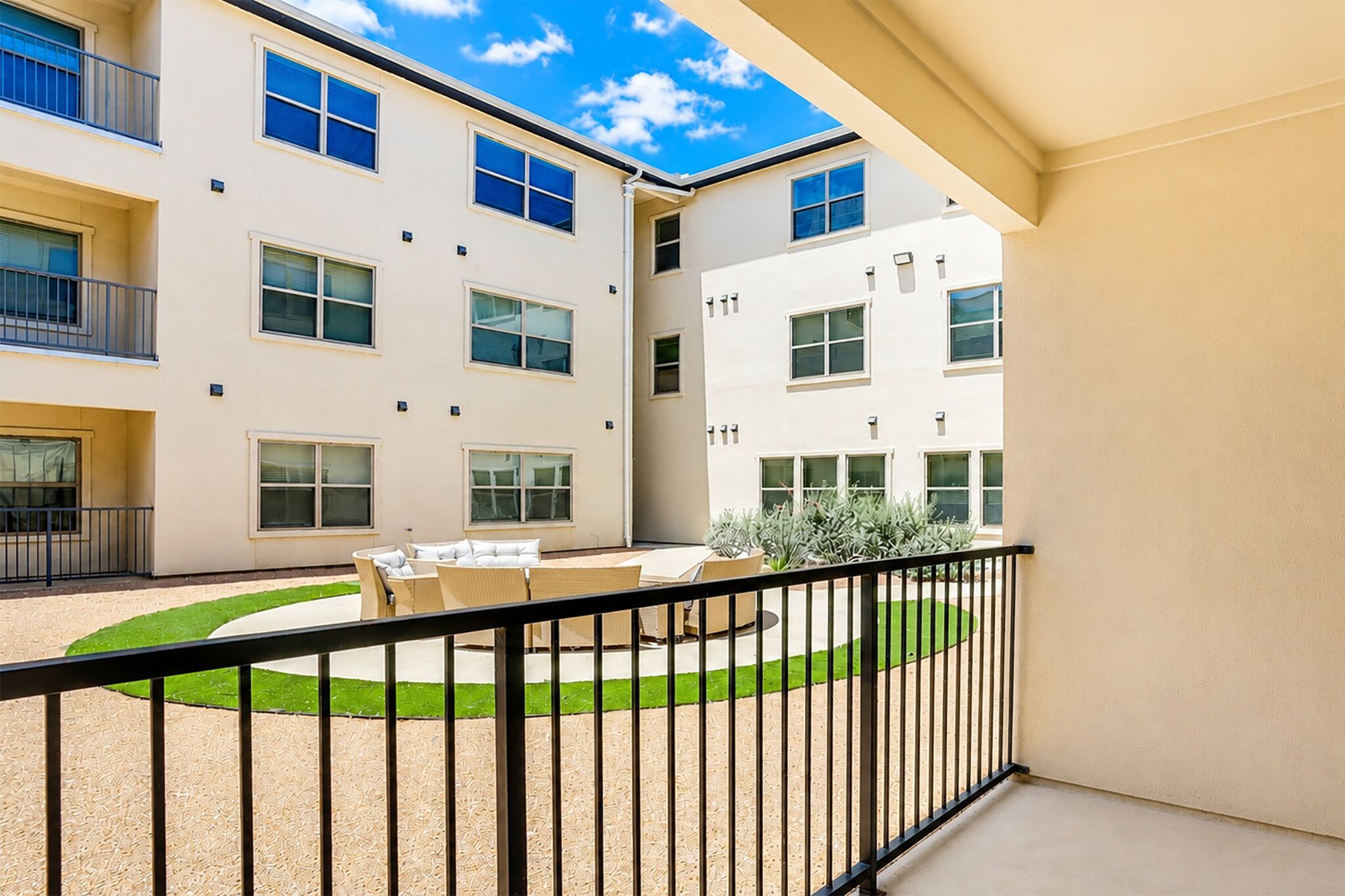A multi-story building with balconies, a courtyard with outdoor furniture, and a clear sky.