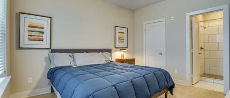 Une chambre à coucher comprenant un lit, une table de chevet, un ventilateur de plafond et une porte donnant sur une salle de bain.