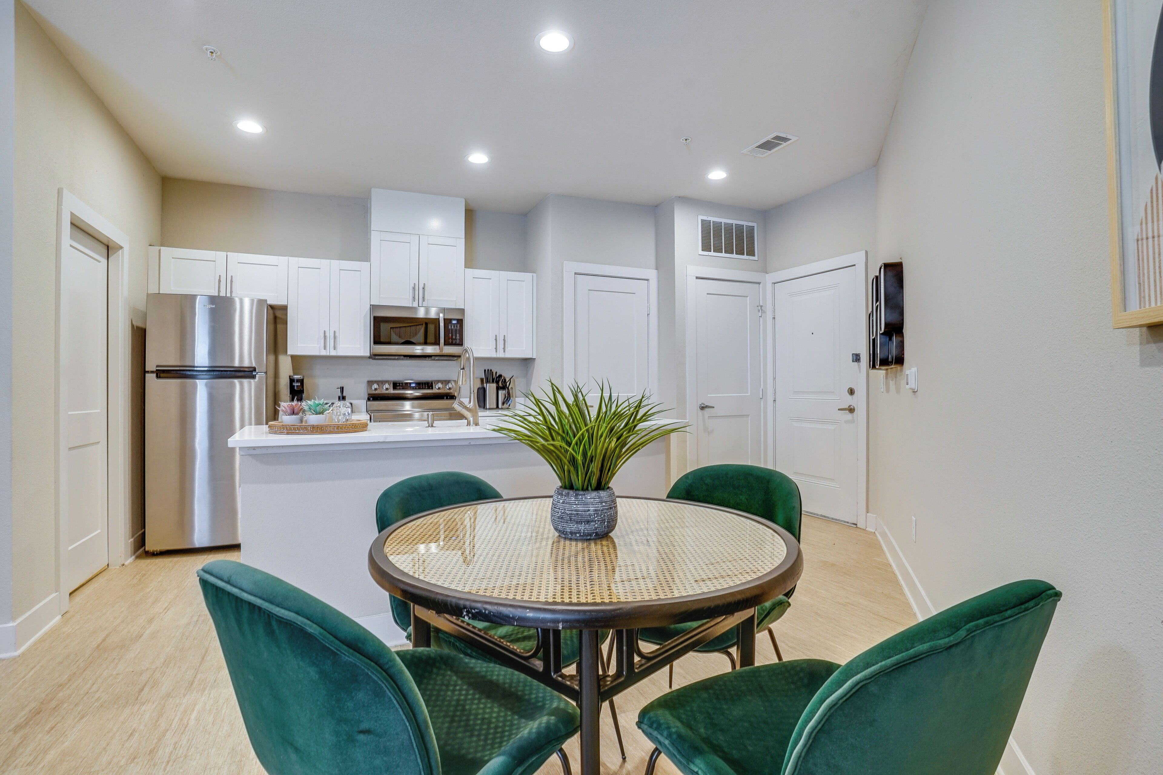 A modern kitchen with white cabinets, a stainless steel refrigerator, a microwave, and a dining area with a round table and green chairs.