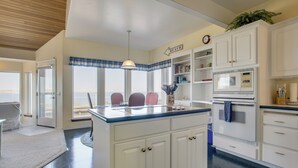 A kitchen with a central island, white cabinetry, a clock, and a view to the outside. - Direct Beach Access! Quiet Diamond Point Retreat (Sequim)