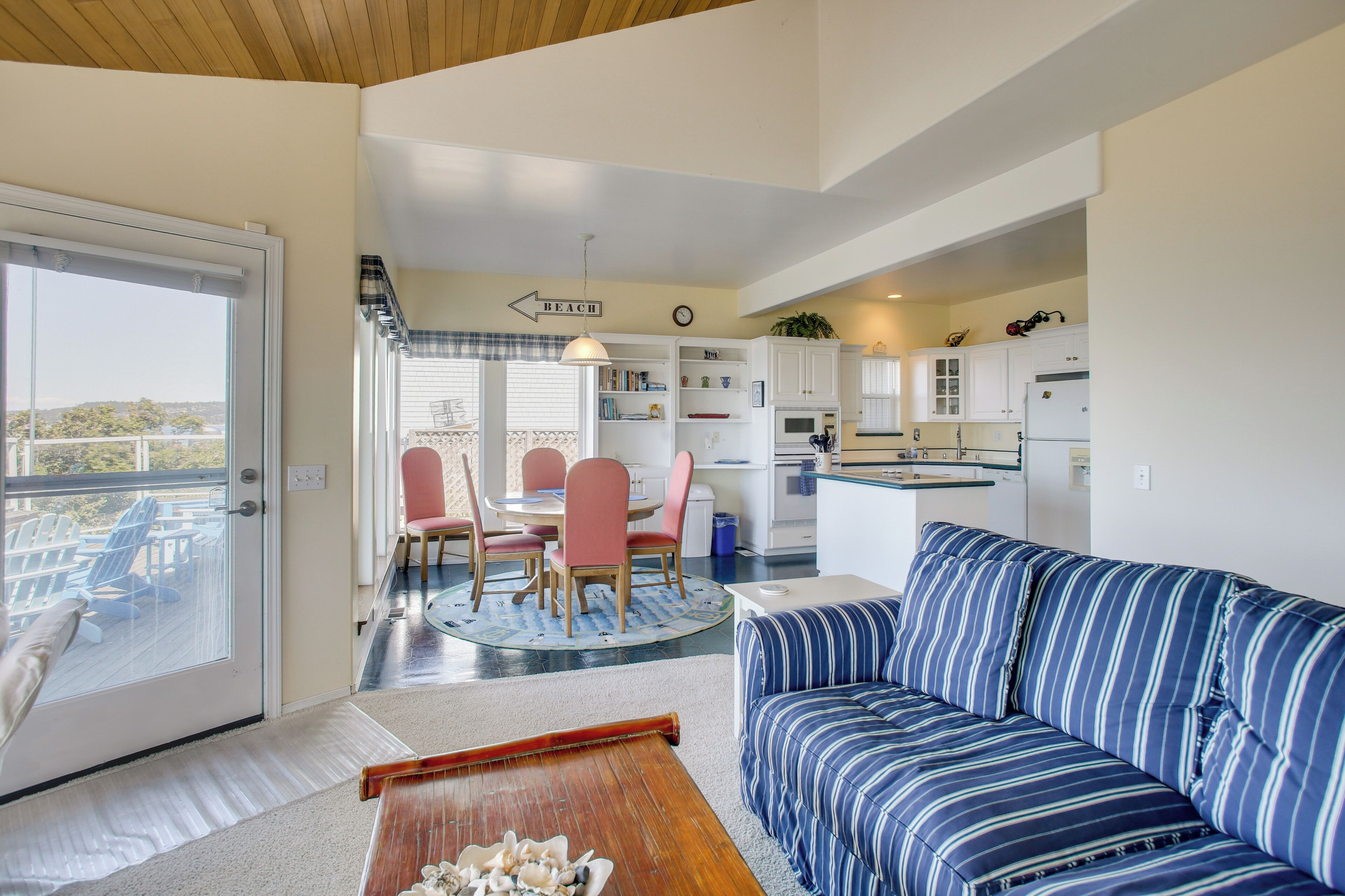 A living room with a sofa, a dining area with chairs, a kitchen with cabinets, and a view of the outdoors.