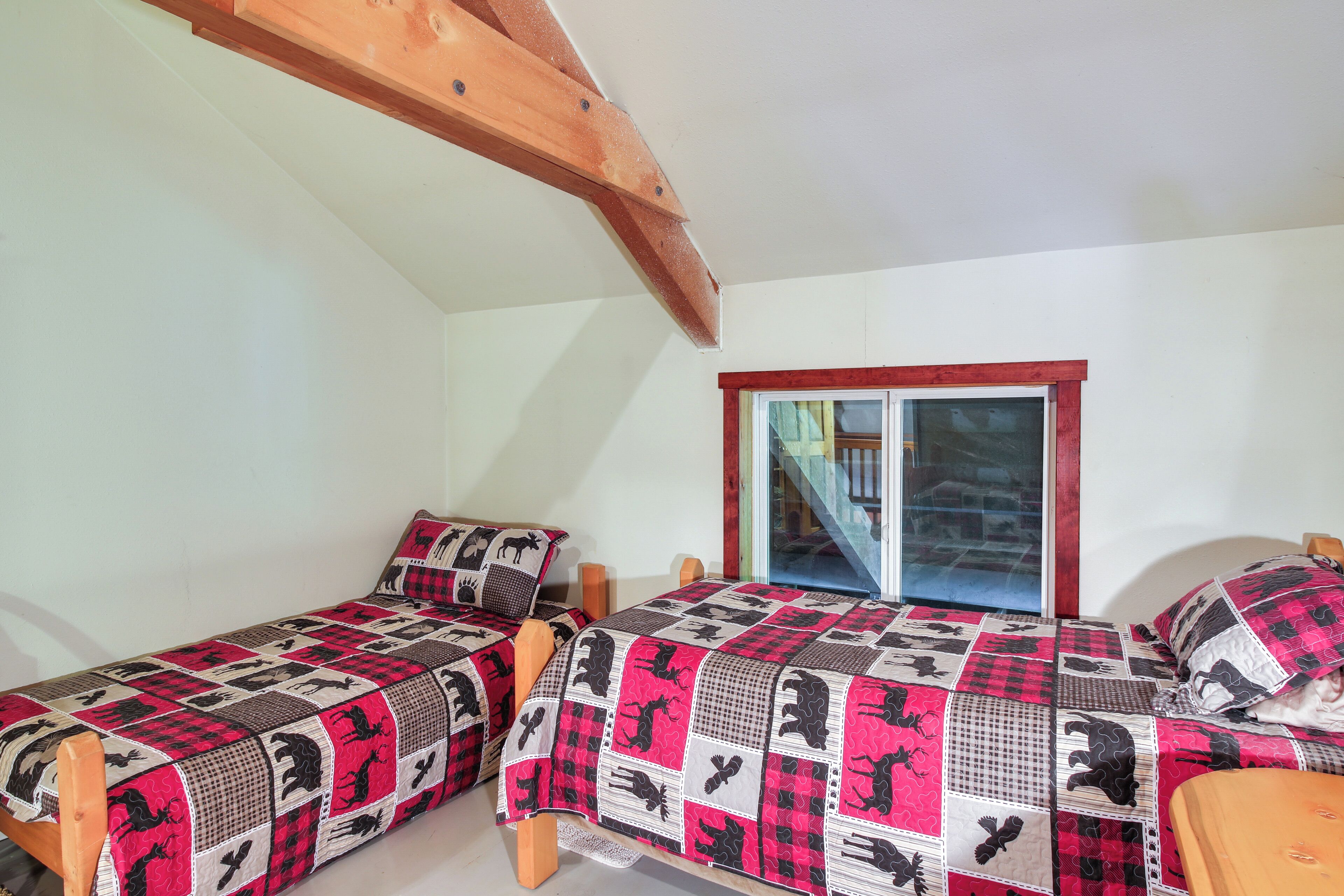 Quarto com duas camas de solteiro, cabeceiras de madeira, janela com moldura vermelha e parede de pedra.