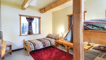 A bedroom with a single bed, a wooden desk, a red rug, and a window with curtains.