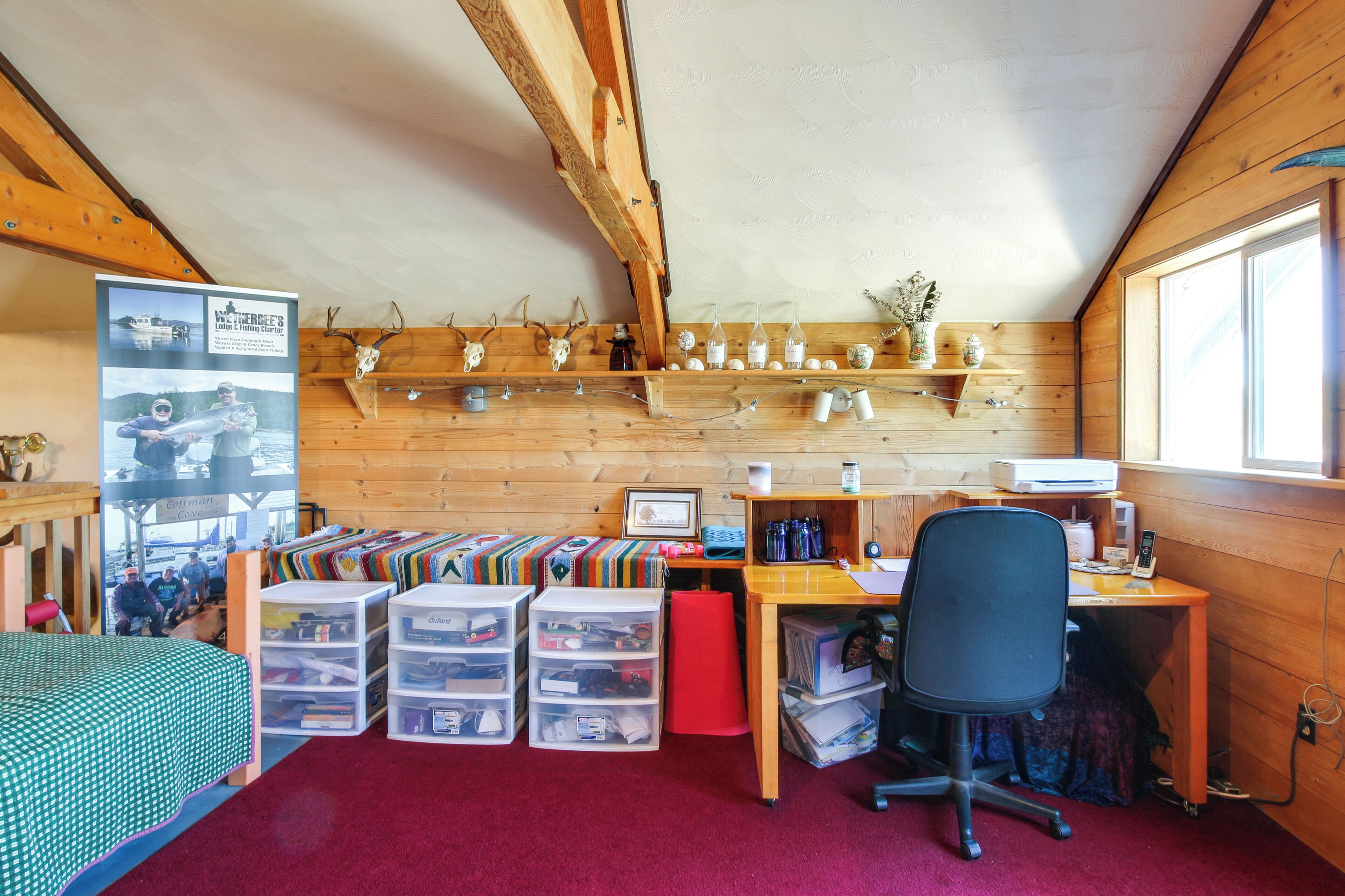 Ein gemütliches Blockhaus mit Holzvertäfelung, einem Schreibtisch mit Computer, Stauraumbehältern und einem Bett mit einem grün gepunkteten Überwurf.