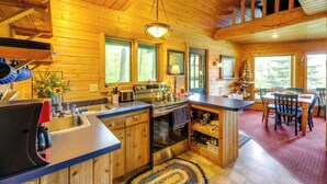 A wooden cabin interior with a kitchen, dining area, and a loft bedroom.