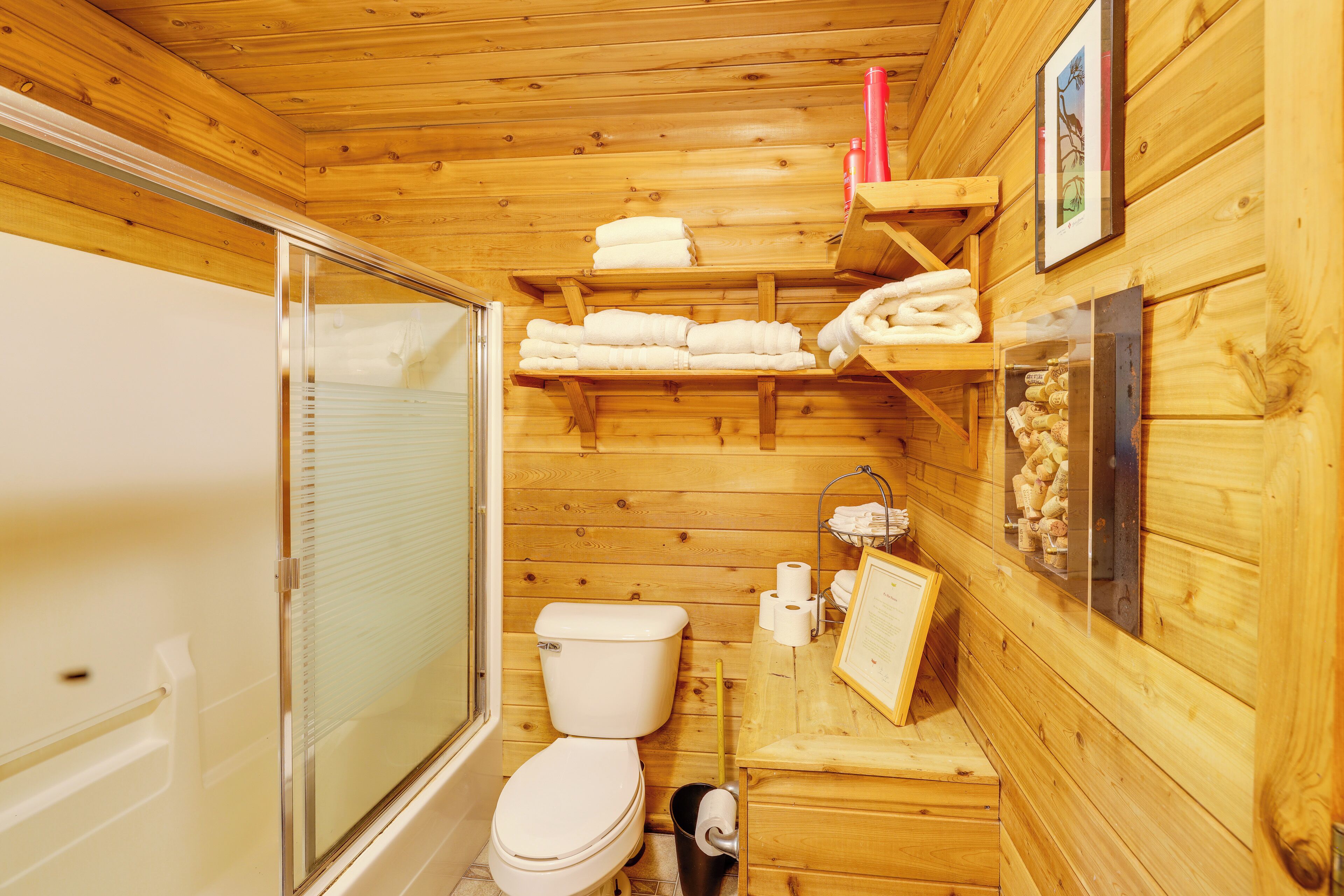A wooden cabin bathroom with a toilet, shower, and shelves with towels.