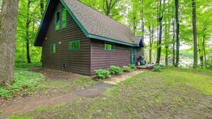 A cabin with a steep roof, a front porch, and a view of a lake surrounded by trees.