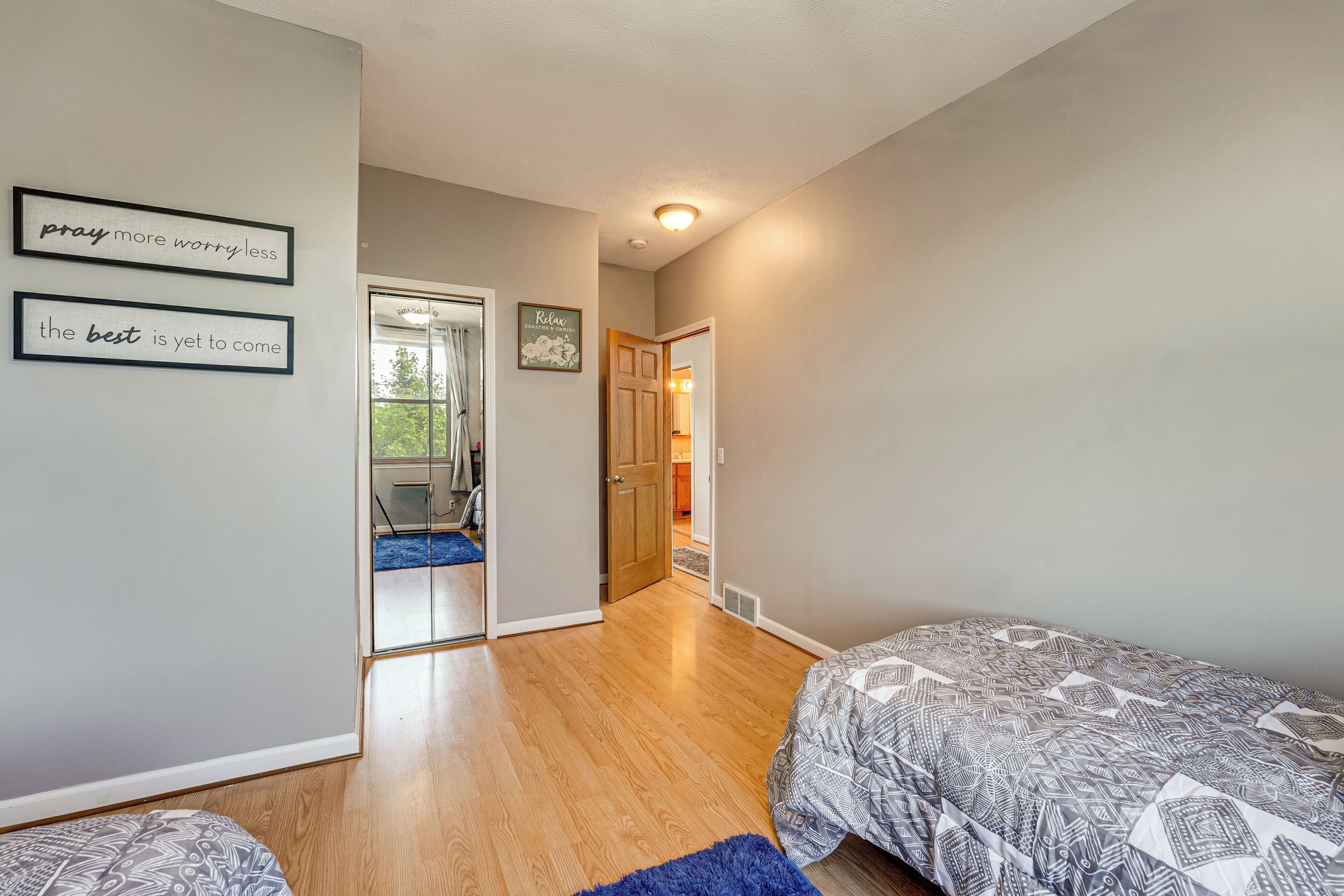 A bedroom with two beds, a blue rug, and motivational wall art.