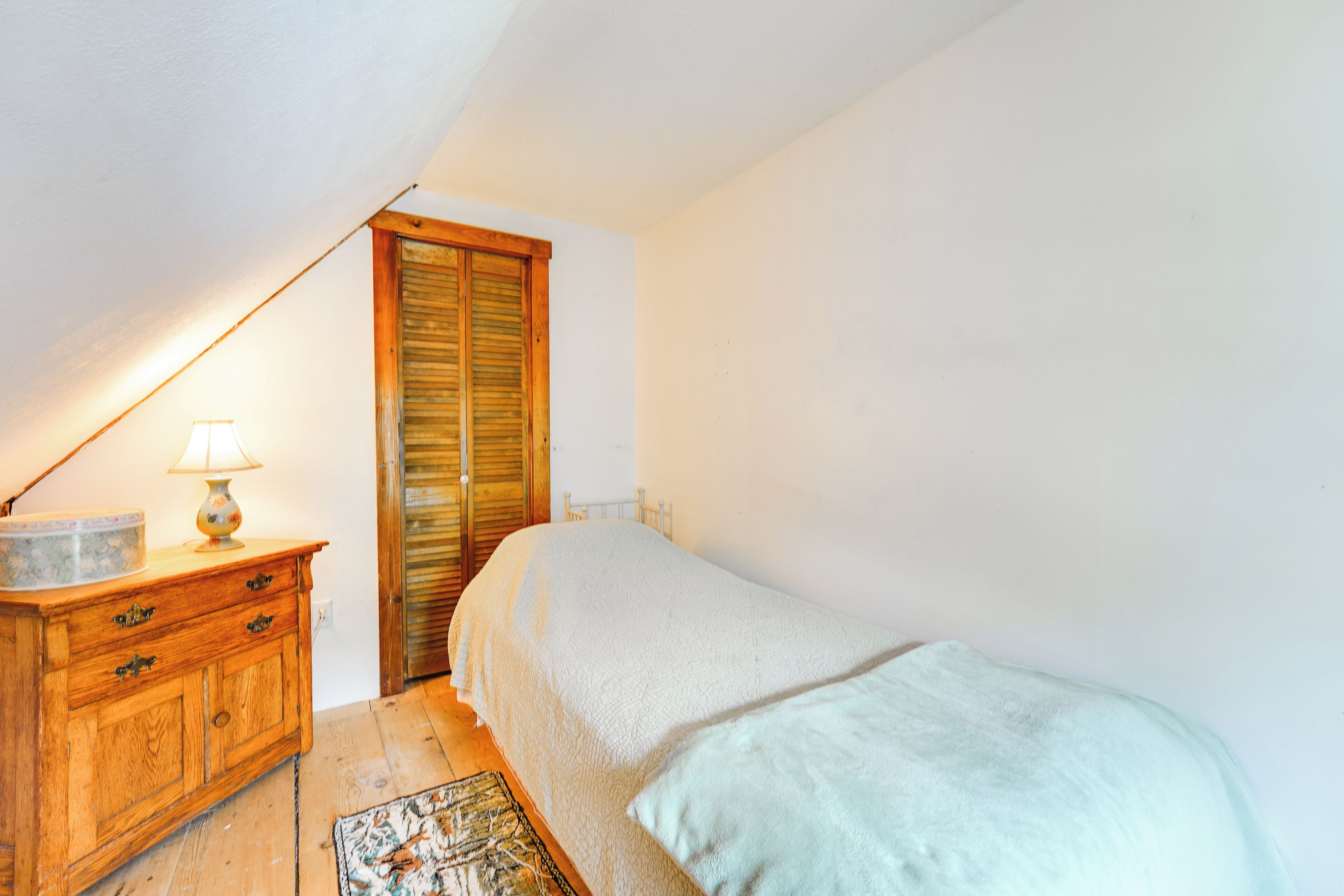 Une chambre à coucher avec un lit, une commode en bois, une lampe et une porte.