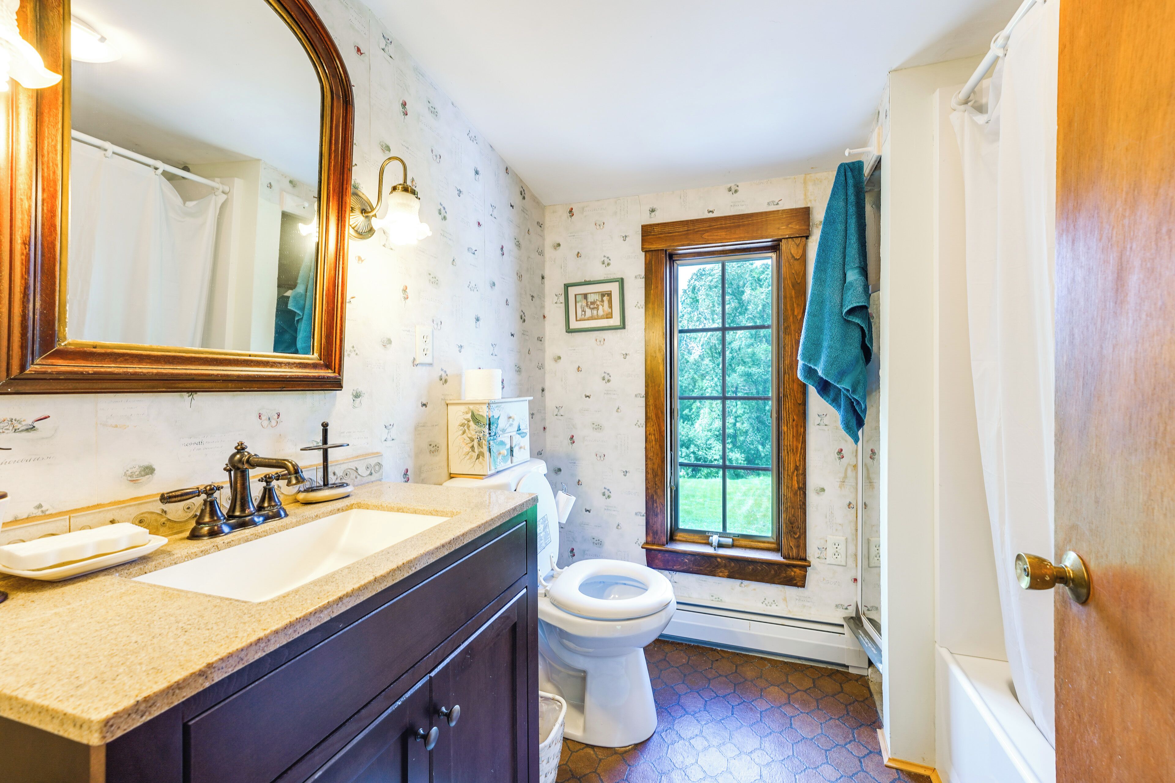 A bathroom with a sink, mirror, toilet, and window.