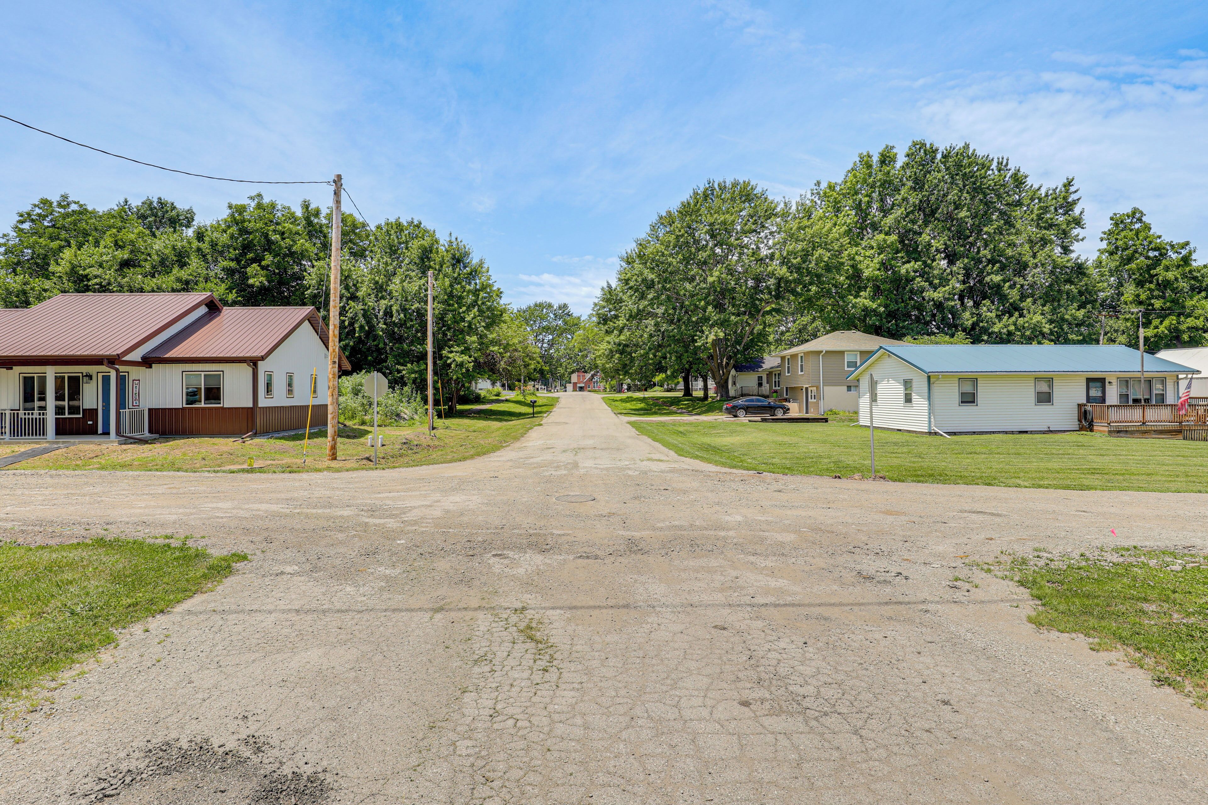 A rural road leading to houses with a dirt path, surrounded by trees and greenery.