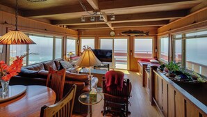 Interior acollidor d'una cabana amb sostre de fusta, un sofà, una taula de dinar i una televisió.