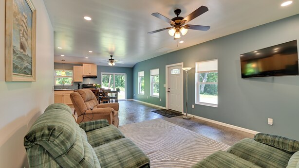 A living room with a sofa, a ceiling fan, a TV, and a view to the kitchen.