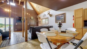 Un comedor con una mesa de madera, sillas blancas y un techo con vigas a la vista.