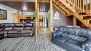 Sala de estar con sofá modular, un sofá adicional, escaleras de madera y una zona de cocina.