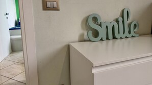 Ett badrum med ett vitt handfat, en väggmonterad ljusströmbrytare och en stor skylt med texten ”Le”.
