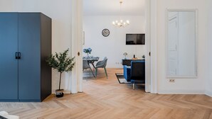 A room with a blue wardrobe, a dining area with chairs and a table, a potted plant, and a TV mounted on the wall. - Grand Living Apartment 150 m² 10 Guests 2 Bathrooms Ku'damm (Berlin)
