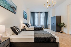 Ett modernt hotellrum med två sängar, en kristallkrona, ett stort fönster med gardiner och en växt.