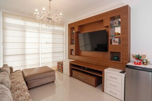 Ein Wohnzimmer mit großem Flachbildfernseher, einer Holzunterhaltungsecke, einem Kronleuchter, einem Sofa und einem Kühlschrank.