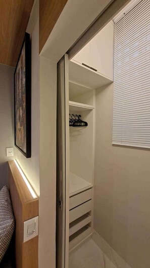 Ein begehbarer Kleiderschrank mit Kleiderstange, Einbauschränken und einem Fenster mit Jalousien.