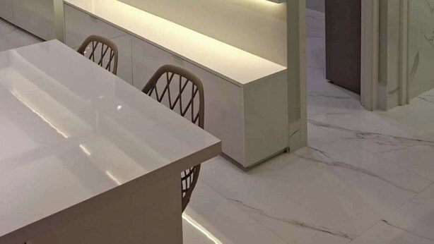 Una cocina moderna con electrodomésticos integrados, un comedor con mesa blanca y un vidrio que da a otra habitación.