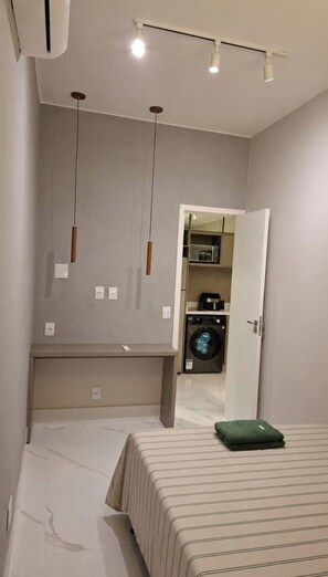 Ein Schlafzimmer mit einem Bett, einem grünen Kopfkissen, einer Waschmaschine und einer Mikrowelle im Hintergrund.