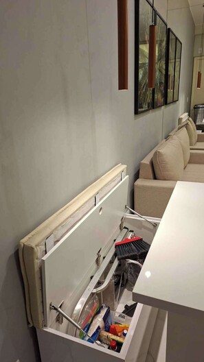 Eine Küche mit einer eingebauten Schublade, einer weißen Arbeitsplatte und einem beigefarbenen Sofa im Hintergrund.