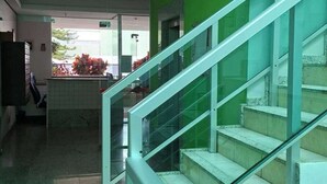 Una escalera con barandillas de vidrio que sube a un piso superior, suelo de baldosas y una pared verde al fondo.