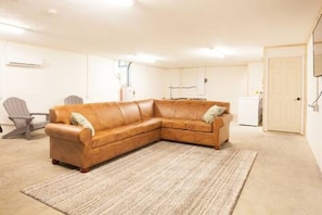 A corner living room with a brown leather sofa, a grey armchair, and a small table. - Charming Home / River Front / Hot Tub / Game Room (Sevierville)