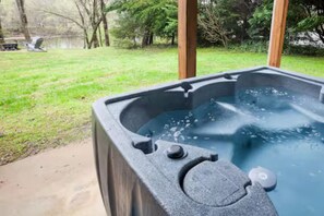 A hot tub with a stone exterior, surrounded by a grassy yard and trees. - Charming Home / River Front / Hot Tub / Game Room (Sevierville)
