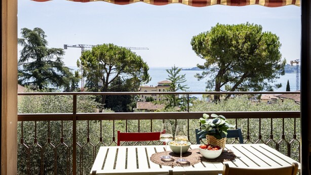 Un balcon avec une table dressée pour deux personnes, donnant sur une étendue d’eau et des arbres.