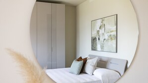 Une chambre à coucher comprenant un lit, des oreillers, une tête de lit, une armoire et un tableau abstrait accroché au mur.
