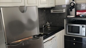 Una cucina con elettrodomestici in acciaio inossidabile, mobili bianchi, un piano di lavoro nero e una parete protettiva rivestita in piastrelle.