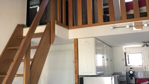 Una cucina con una scala in legno, mobili bianchi, un frigorifero e un forno a microonde.