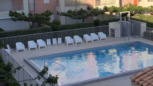 Una piscina con lettini, un'area recintata e edifici a più piani con balconi.