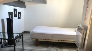 Una stanza con un letto, un tavolo e un termosifone, e un condizionatore d'aria a parete.