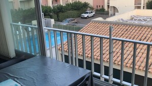 Un balcone con vista su una piscina, un'auto parcheggiata e edifici vicini.