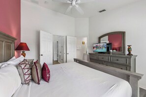 Ein Hotelzimmer mit einem großen Bett, einem Schminktisch, einem Fernseher und einem Deckenventilator.