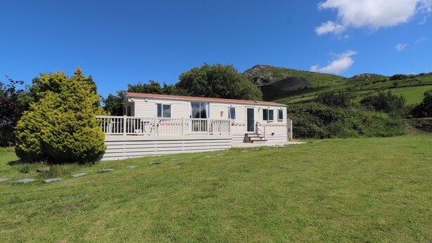 A single-story mobile home with a porch, a small deck, and a front door. - Mor a Mynydd (Pwllheli)