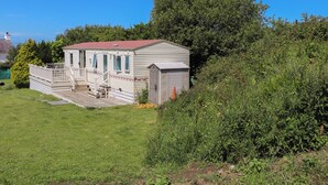 A mobile home with a porch, a small shed, and a grassy yard. - Mor a Mynydd (Pwllheli)
