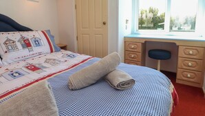 A bedroom with a bed, a desk, a window with a view, a door, and a shelf with a book. - Mor a Mynydd (Pwllheli)