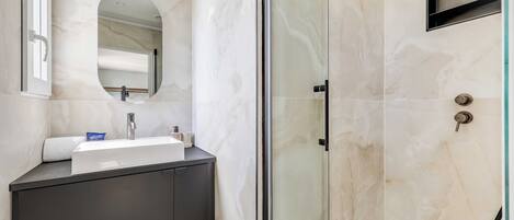 A bathroom with a glass shower enclosure, a sink with a mirror, and a dark-toned cabinet.