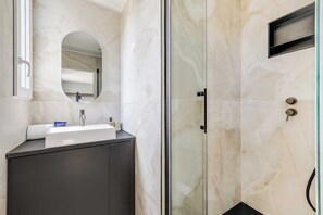 Ein Badezimmer mit Duschkabine aus Glas, Waschbecken mit Spiegel und einem dunklen Schrank.