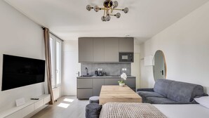 A modern hotel room with a flat-screen TV, a sofa, a wooden coffee table, a bed, a small kitchen area, and a large mirror. - Modern Studio 3P - Aubervilliers (Aubervilliers)