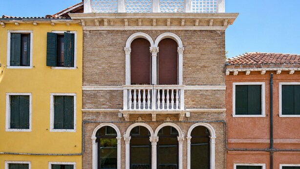 Un edificio de varios pisos con balcón, ventanas en arco y techo de tejas.